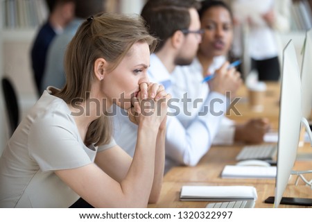 Upset frustrated and confused female worker folding hands on chin feels puzzled having problem troubles and doubts about business moments, sitting in shared modern office with multinational coworkers Royalty-Free Stock Photo #1320322997