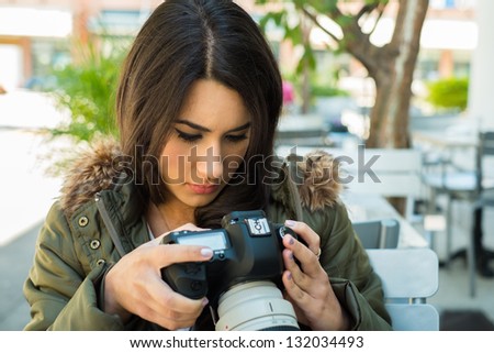 Beautiful young woman outdoors looking at pictures on a camera display.