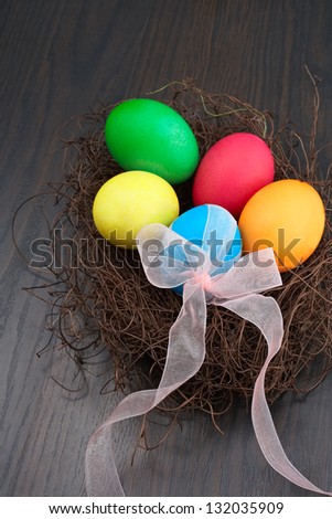 Colorful Easter eggs in a nest with bow and ribbon on the wooden table