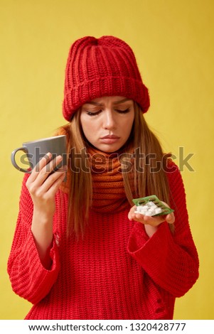 Sick woman holding pills and a cup in her hands. Image on yellow background.