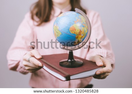 Young woman holding a brown agenda and small globus on gray background 