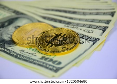 Gold bitcoins and hundred dollar bills lie on a white background