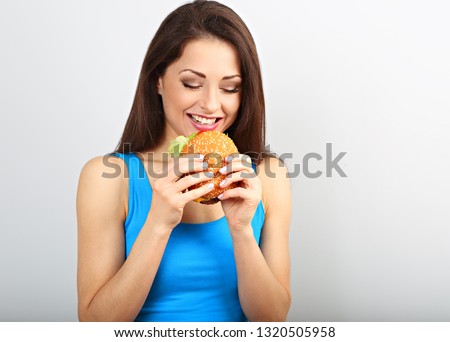 Excited happy hungry woman wanting to bite tasty burger on blue background. Closeup portrait