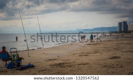 Ann angler sitting in front of fishing rods in front of the Mediterranean Sea. The photo was taken on San Antonio beach in the seaside holidays town of Cullera, in Valencia, Spain, Europe.