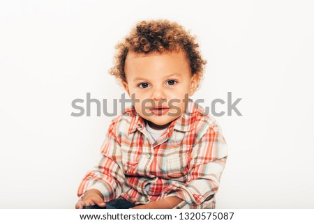 Studio shot of handsome african toddler boy wearing orange plaid shirt, posing on white background