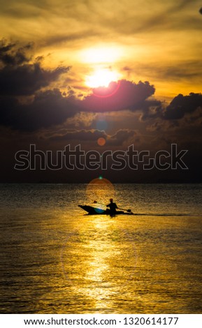 Silhouette of fisherman rowing the boat while sunset.