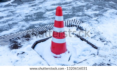 Orange caution cone in snow on sidewalk