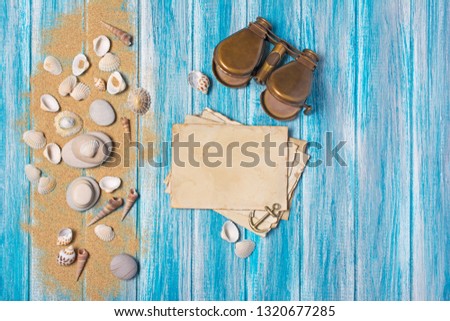 Top view on mock-up of vintage photo cards and binoculars with seashells on sand and blue wooden background