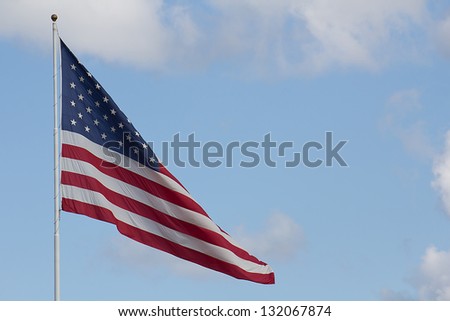 American flag on pole against baby blue sky with light clouds and large open area for background use.