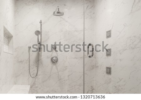 Modern white shower with marble looking porcelain tiles, built-in seat and recessed shampoo holder and glass shower door Royalty-Free Stock Photo #1320713636