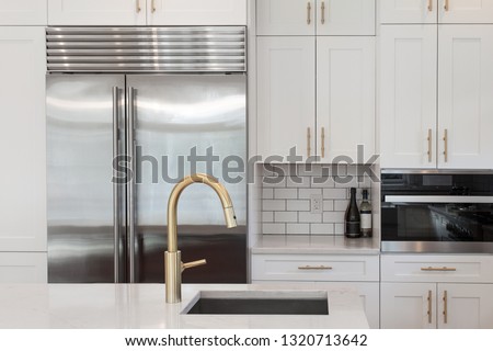 White kitchen built with shaker style cabinets and white granite. Shows stainless steel oven, subway tile back splash and  refrigerator. Brushed gold faucet and hardware Royalty-Free Stock Photo #1320713642