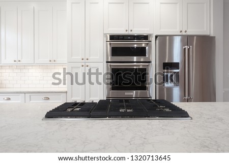 White kitchen built with shaker style cabinets and white granite. Shows stainless steel oven, subway tile back splash and cook-top and refrigerator  Royalty-Free Stock Photo #1320713645