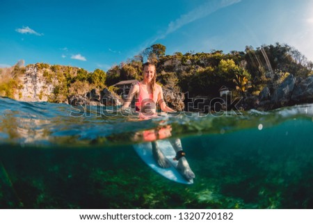 Attractive surfer girl with surfboard. Surfer sit at board in ocean.