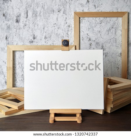 Blank white canvas for painting, a wooden easel and stretcher bars on table