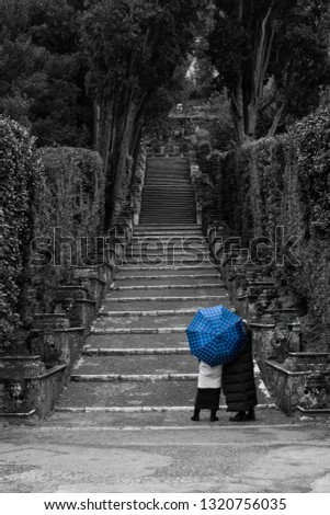 Two girls looking at the stairway with a blue umbrella. Edited with a selective blue color and black and white