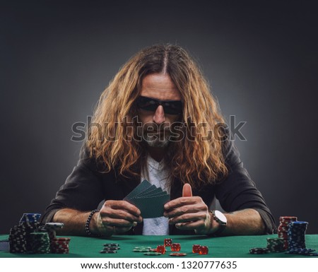 Long-haired handsome man playing poker in a casino. Studio concept on gray background