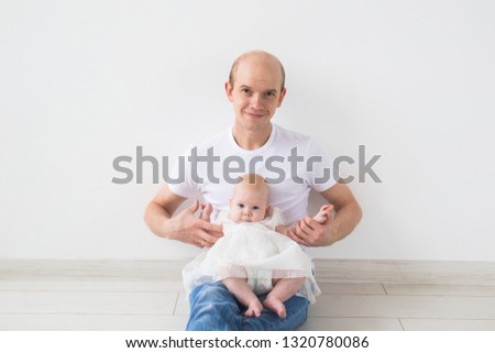 Infant baby, fatherhood and children concept - happy bald father with little daughter on his knees on white background