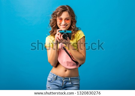 attractive smiling happy woman posing with vintage photo camera taking pictures dressed in hipster summer colorful outfit isolated on blue studio background, traveler photographer hobby