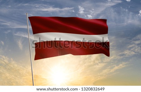 Latvia flag waving in the wind against a blue sky and clouds