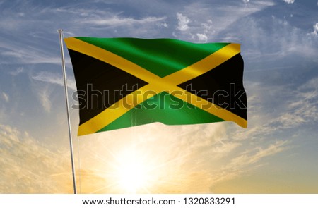 Jamaica flag waving in the wind against a blue sky and clouds