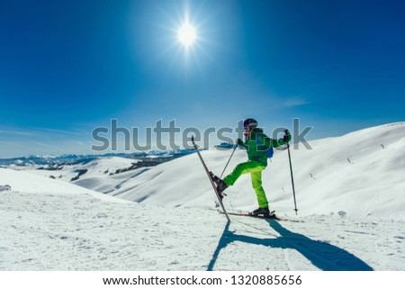 Skier standing with one raised leg on a ski slope at a sunny day and looking somewhere 