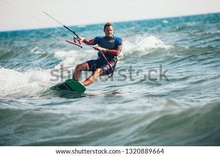 Professional kiter makes the difficult trick on a beautiful background. Kitesurfing Kiteboarding action photos man among waves quickly goes Royalty-Free Stock Photo #1320889664