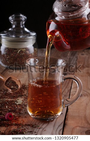 A stream of rooibos tea pouring from the teapot to a transparent glass cup