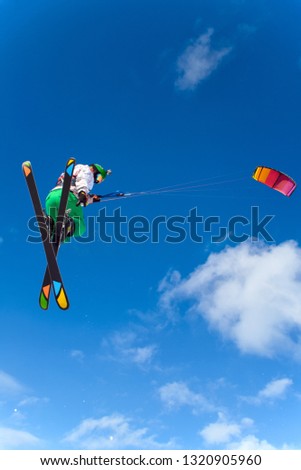 Professional kite boarding rider sportsman with kite in blue sky jumps high acrobatics kiteboarding trick. Extreme outdoor activities in winter. Concept sports snowkite, snowkiting ski snowboard