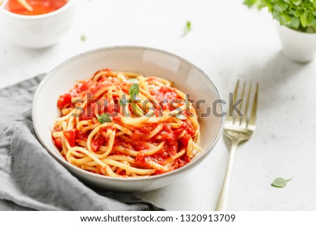 Traditional pasta with tomato and Greek basil sauce in a ceramic bowl on a white table. 