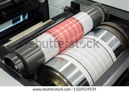 Flexography printing process on in-line press machine. Photopolymer plate stuck on printing cylinder, substrate is sandwiched between the plate and the impression cylinder to transfer the ink. Royalty-Free Stock Photo #1320924929