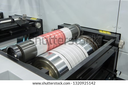 Flexography printing process on in-line press machine. Photopolymer plate stuck on printing cylinder, substrate is sandwiched between the plate and the impression cylinder to transfer the ink. Royalty-Free Stock Photo #1320925142