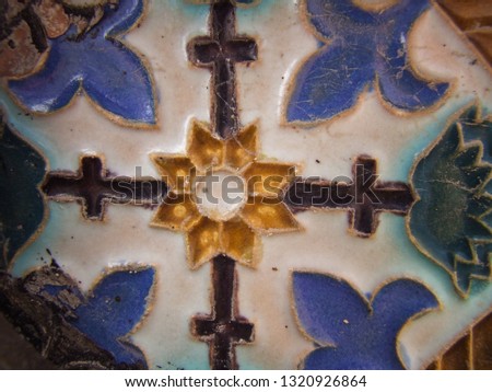 old ceramic tile with texture and drawings of flowers and geometric in color