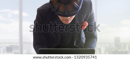 Young successful business man standing and working on laptop desktop computer. Handsome man at modern workspace office are focusing on work. Isolated background with blurry windows, natural expression