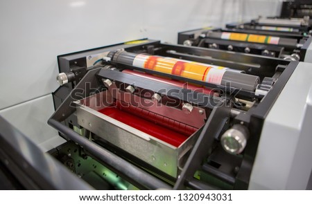 Flexographic printing machine with an ink tray, ceramic anilox roll, doctor blade and a print cylinder with polymer relief plate stuck on it. In-line press machine. Rotary or Flexo printing machine. Royalty-Free Stock Photo #1320943031