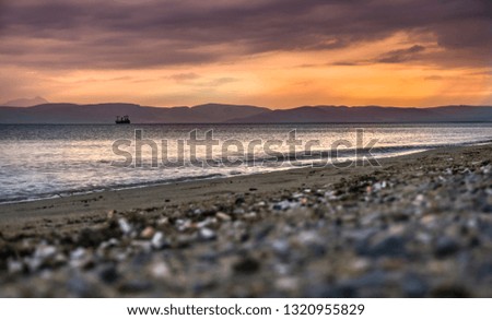 Dramatic sunset background. Sun going down on sea horizon & pebble beach. Beautiful blazing sunset landscape at blue sea and orange sky above it with awesome sun golden reflection on calm waves.
