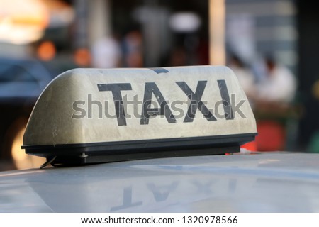 Taxi light sign or cab sign in drab white color and black text on the car roof at the street blurred background, Myanmar.
