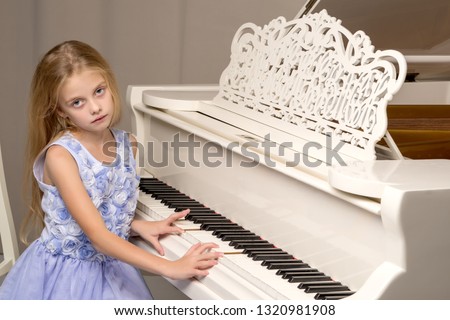 Beautiful little girl near a white grand piano. The concept of education and school, children's creativity.