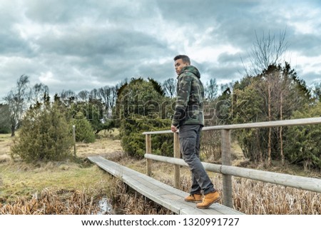 A young guy are hiking in a nature reserve in Sweden and goes over a creek in outdoor clothing