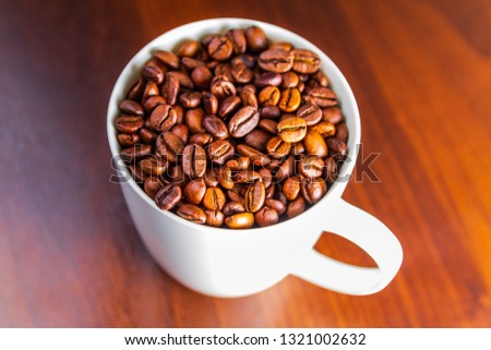 Roasted Coffee beans in a white mug cup isolated on a rustic wood table