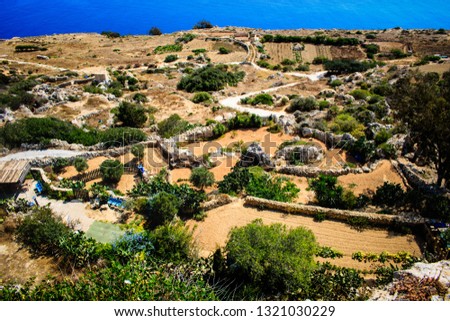 
The picture is a beautiful path that leads through a sandy yellow mountain surrounded by green trees all the way to the sea. this beautiful picture was made in Malta