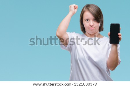 Young adult woman with down syndrome showing smartphone screen over isolated background annoyed and frustrated shouting with anger, crazy and yelling with raised hand, anger concept