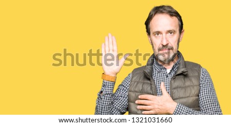Middle age handsome man wearing winter vest Swearing with hand on chest and open palm, making a loyalty promise oath
