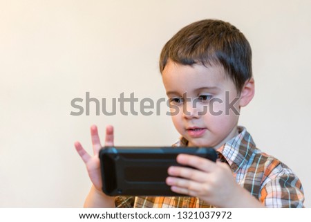 Portrait of a smiling little boy holding mobile phone isolated over light background. cute kid playing games on smartphone