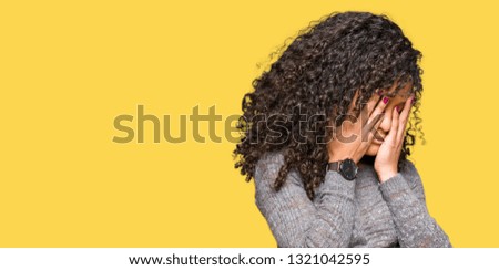 Young beautiful woman with curly hair wearing grey sweater with sad expression covering face with hands while crying. Depression concept.
