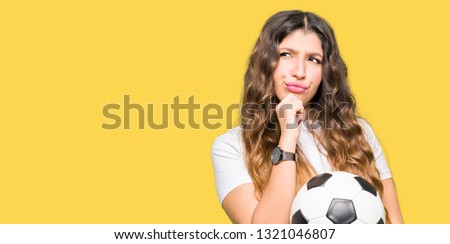 Young adult woman holding soccer football ball serious face thinking about question, very confused idea
