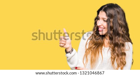 Young beautiful woman wearing white sweater Looking proud, smiling doing thumbs up gesture to the side