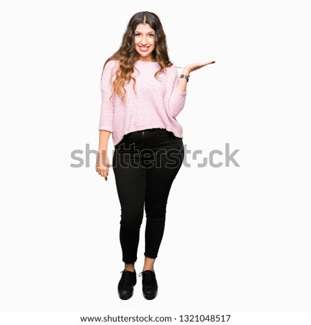 Young beautiful woman wearing pink sweater smiling cheerful presenting and pointing with palm of hand looking at the camera.