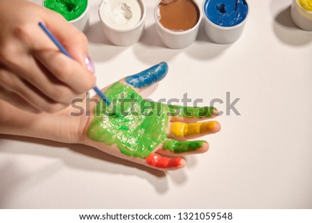 Little girl paints her hands with finger paint on white background. Bright colours