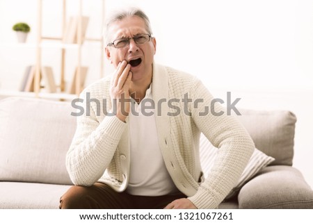 Senior man having toothache and touching cheek, suffering from tooth pain, caries