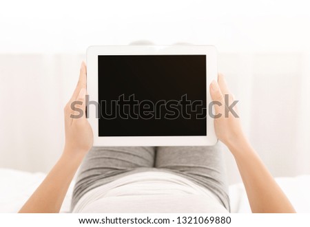 Young woman using digital tablet with blank screen, scrolling pages, lying on bed at home, mockup, pov